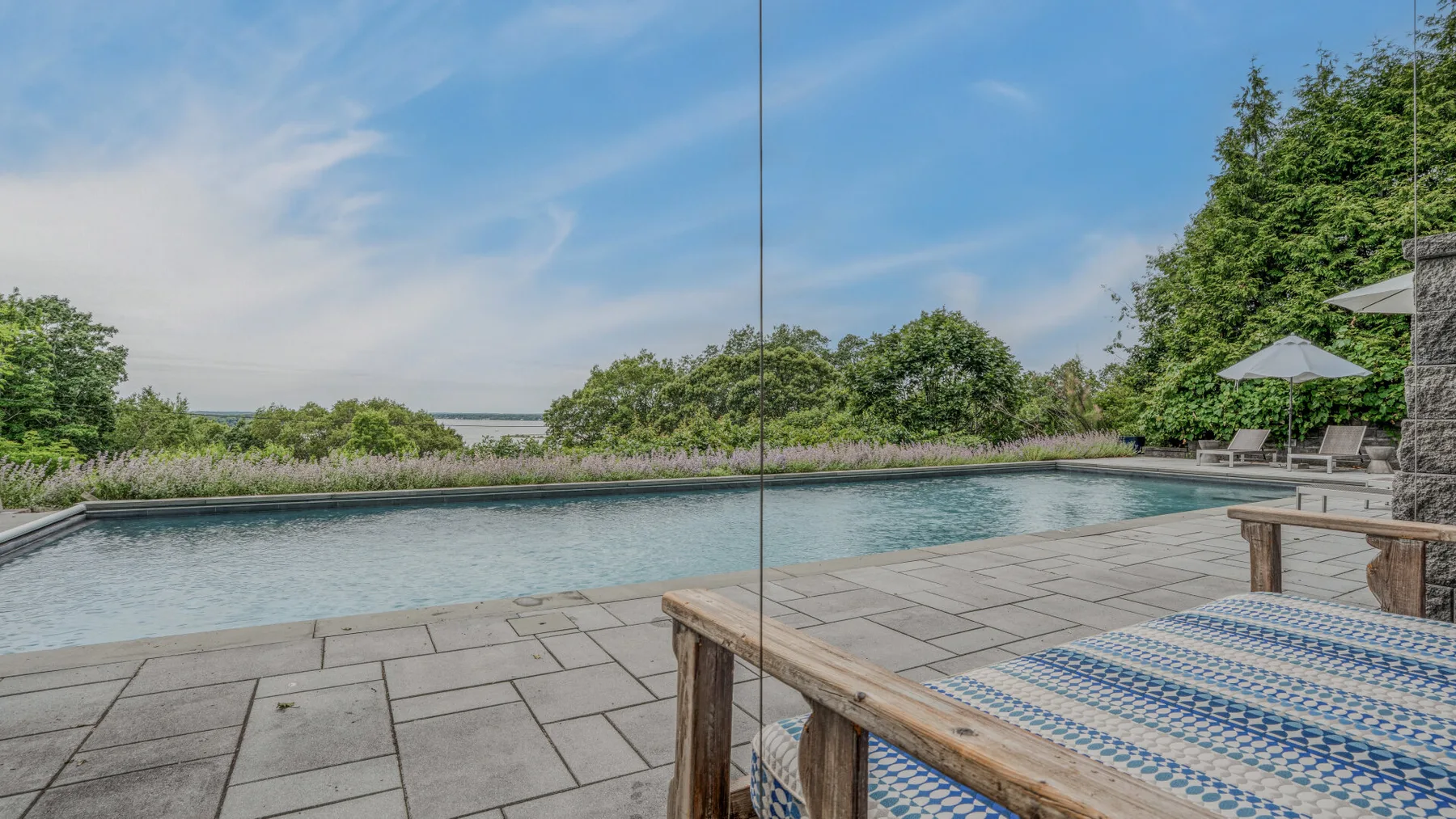 An outdoor swimming pool bordered by a stone patio and green landscaping.