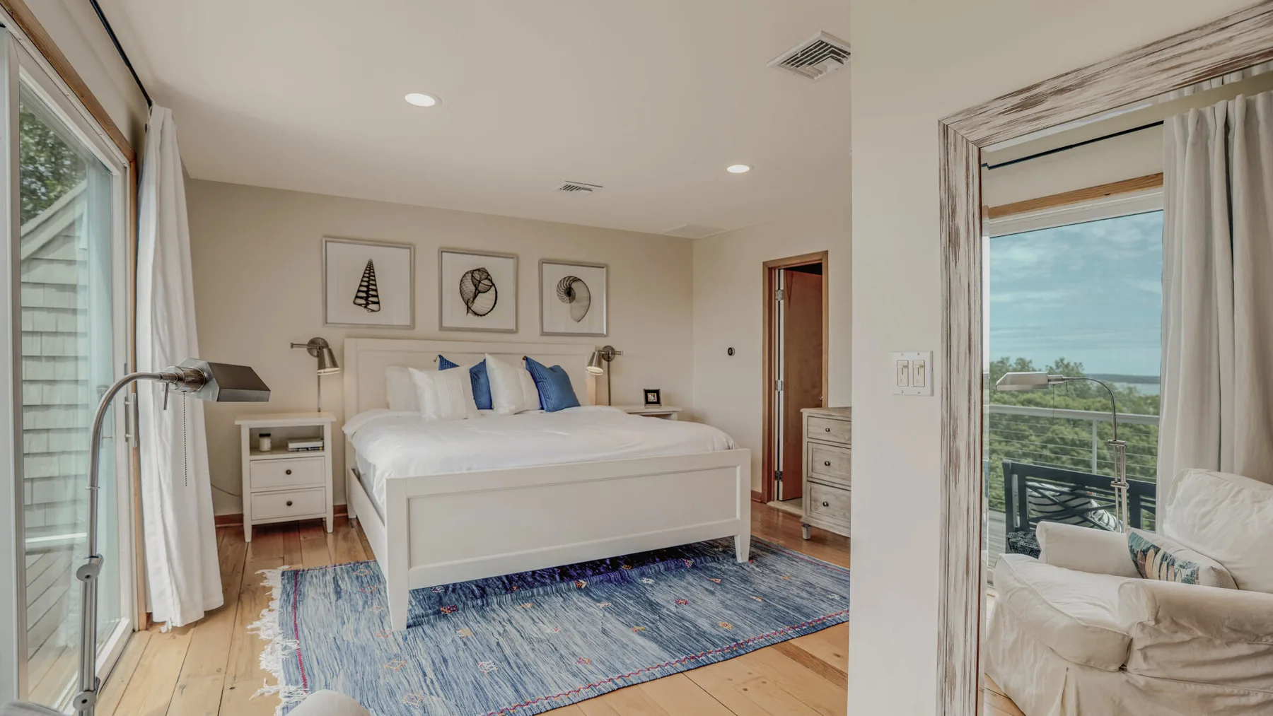 A bedroom with a bed, blue accents, and large windows opening onto a balcony.
