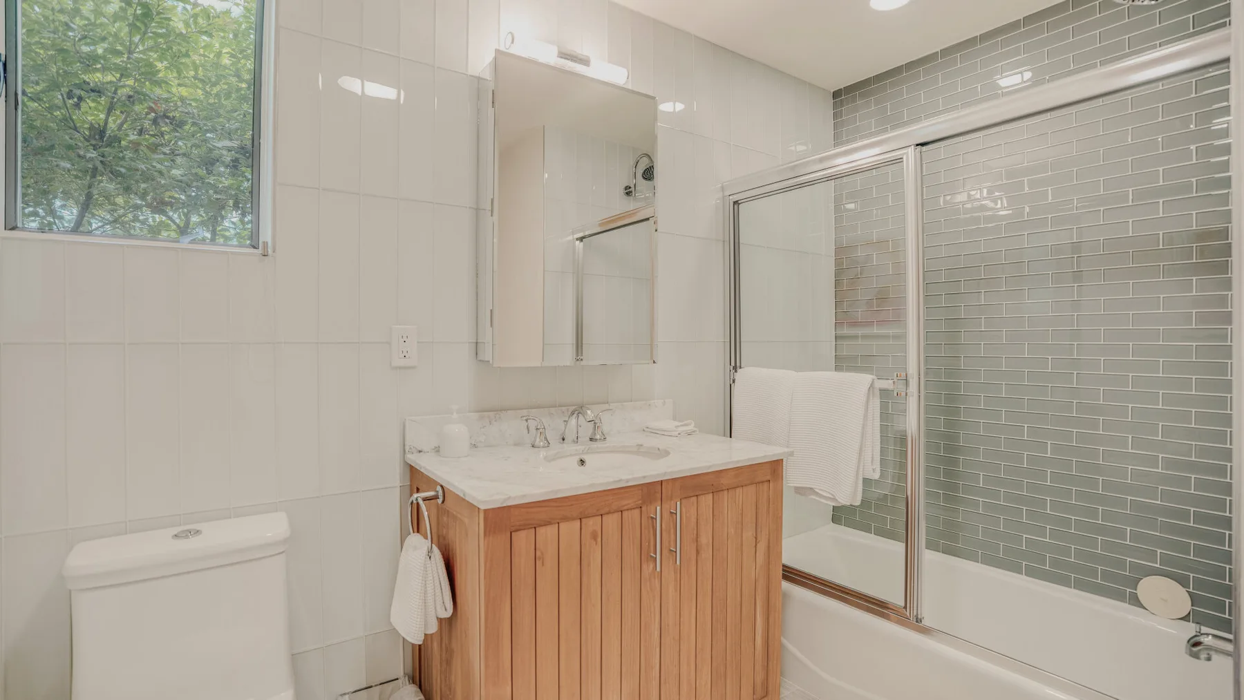 A bright bathroom with a wood-front vanity and glass shower.