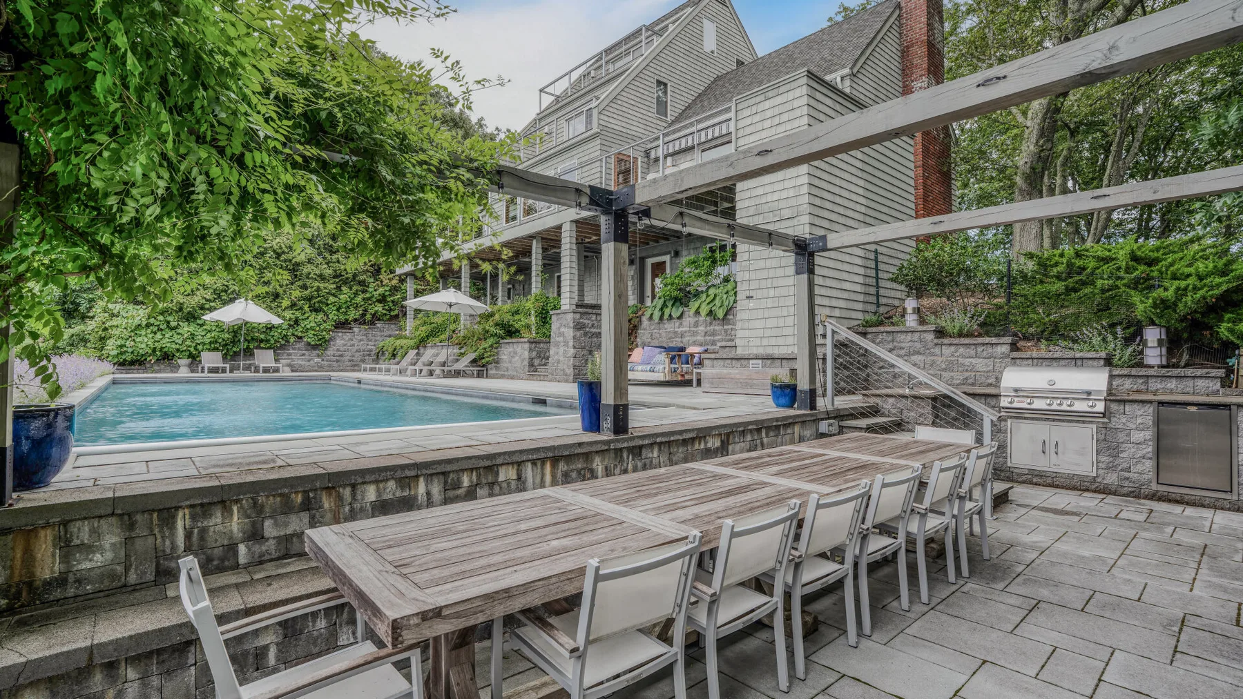 A patio dining area beside a swimming pool and a large house.