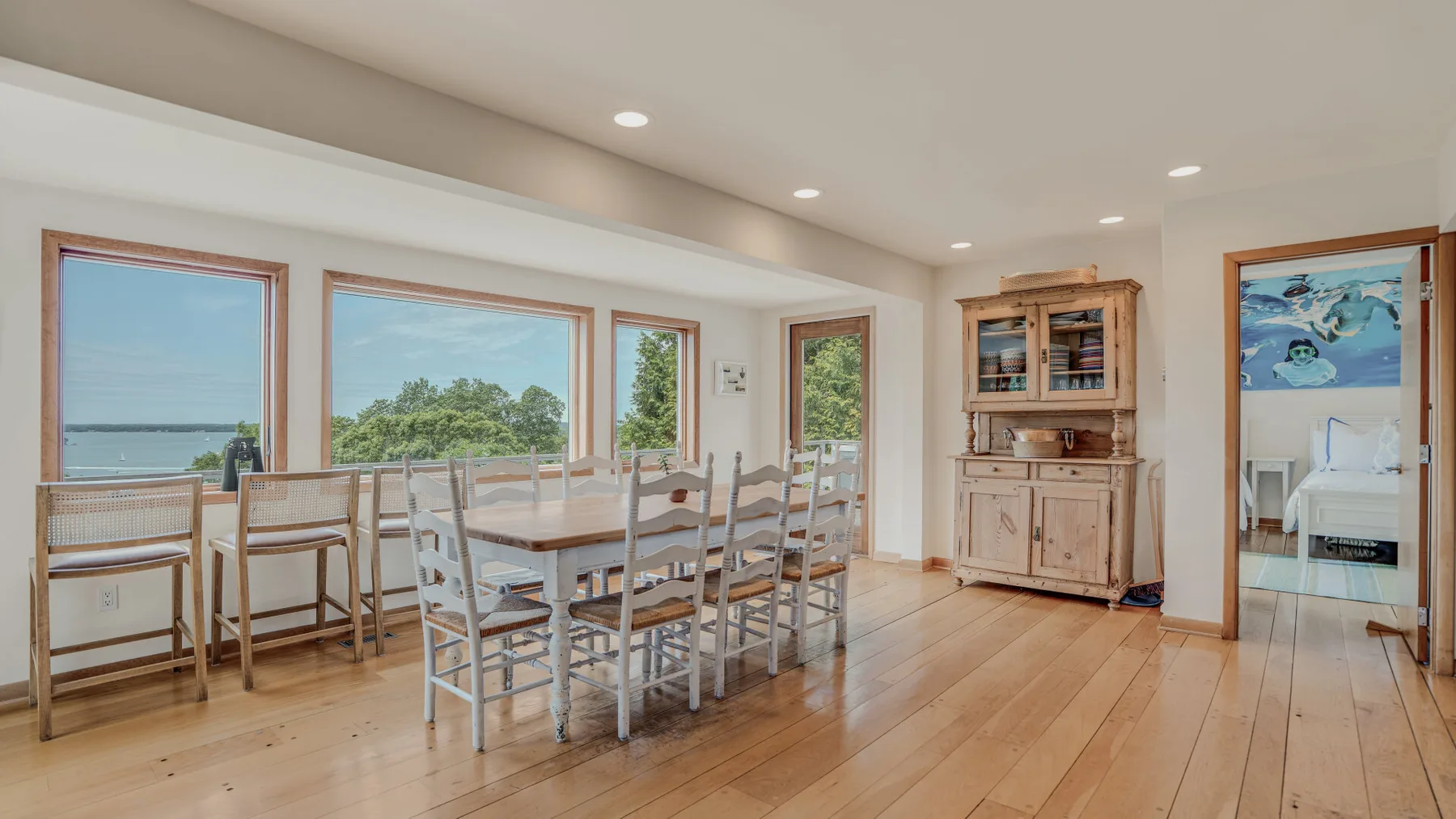 A bright dining area with a long table and large windows overlooking the water.