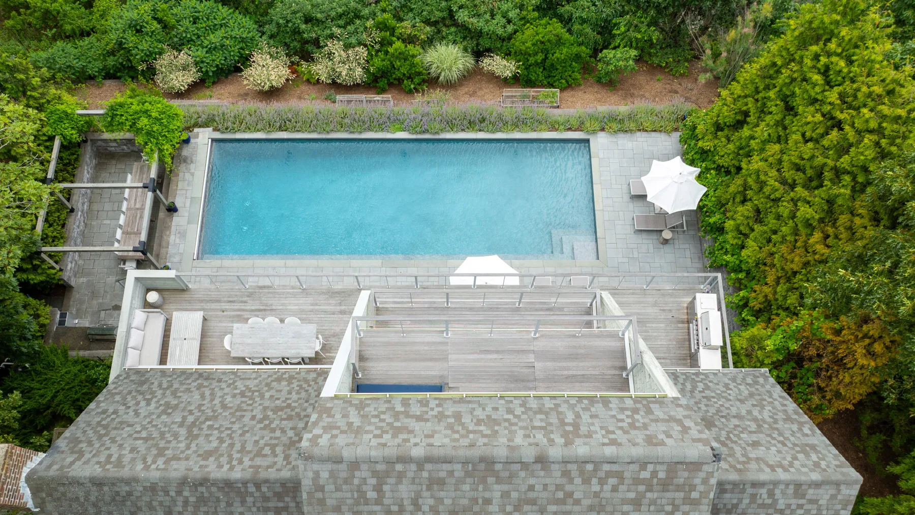 An outdoor swimming pool is surrounded by a paved deck and greenery.