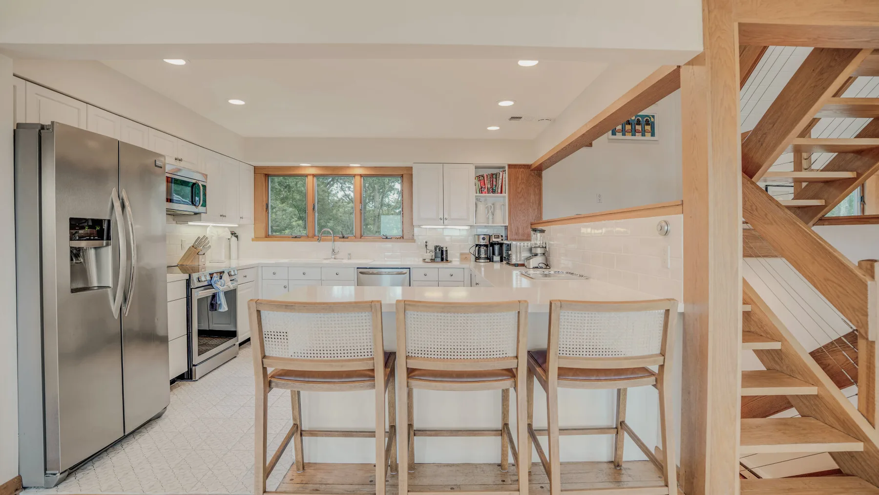 A bright kitchen with a central island and wooden stairs beside it.
