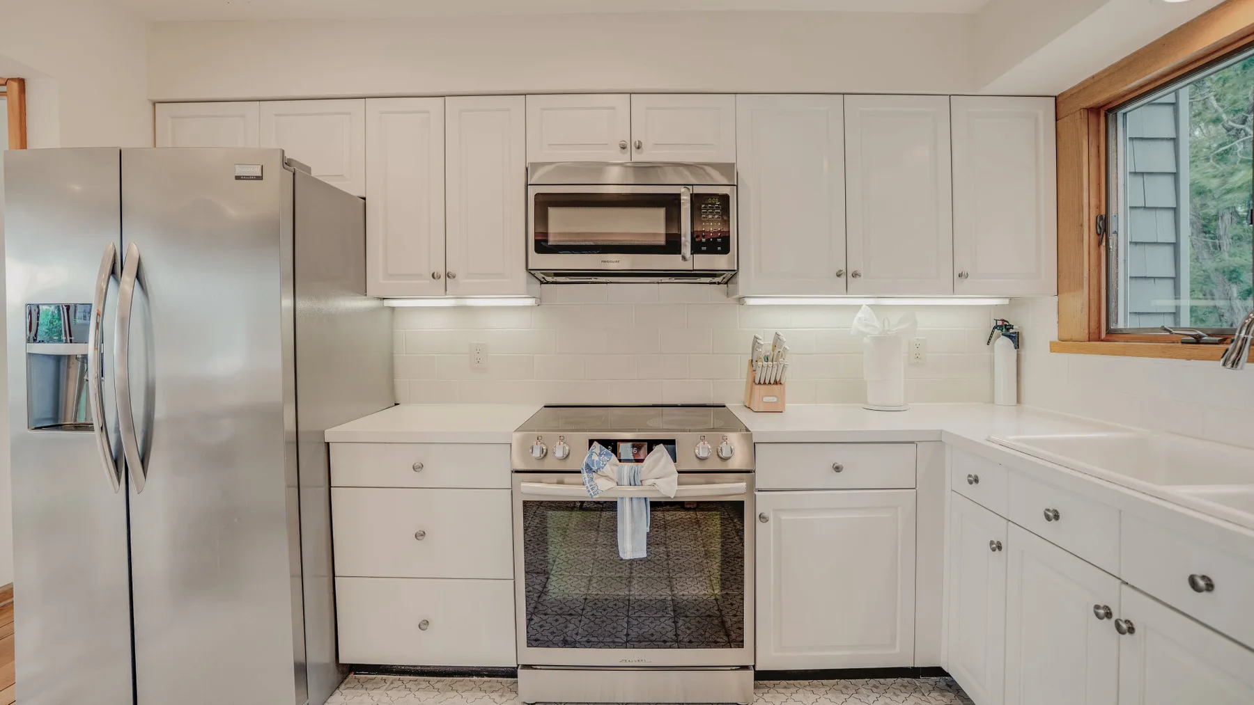 A bright kitchen with white cabinetry, stainless steel appliances, and a window.