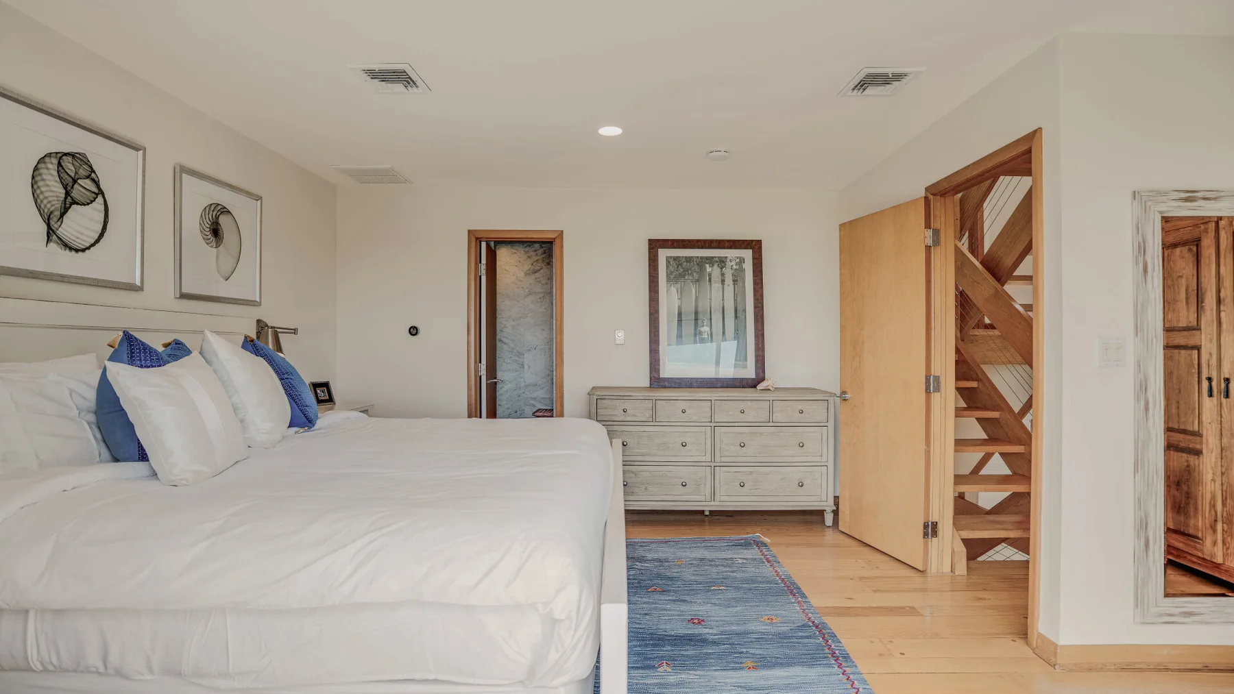A bedroom with a large bed, a dresser, and a blue rug.