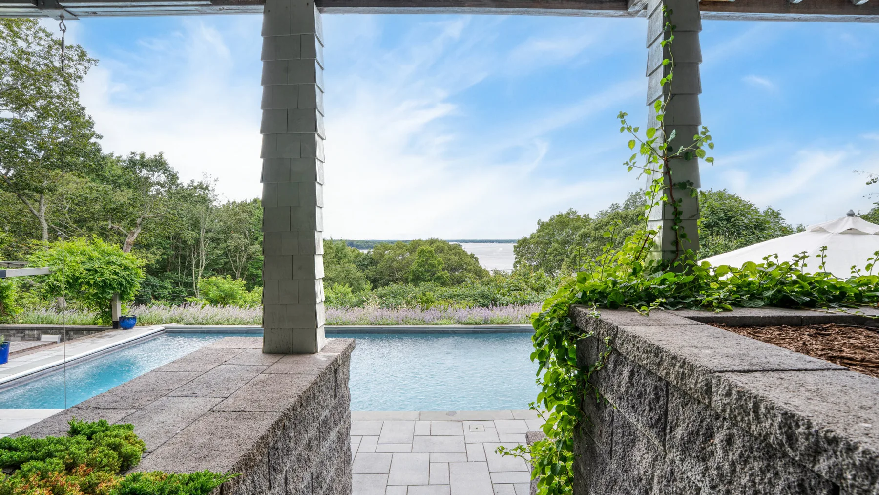 A swimming pool sits beside a paved patio with views of green trees.
