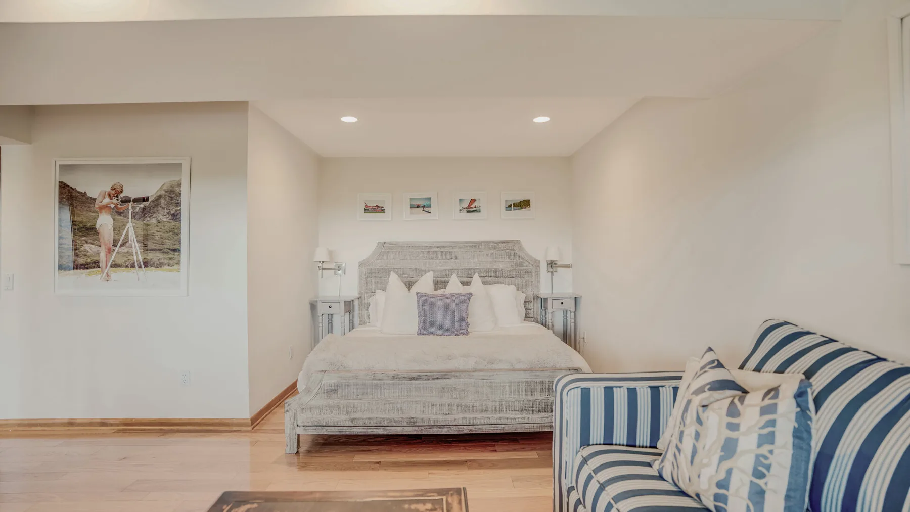 A bright bedroom with a made bed and a blue-and-white striped seating area.