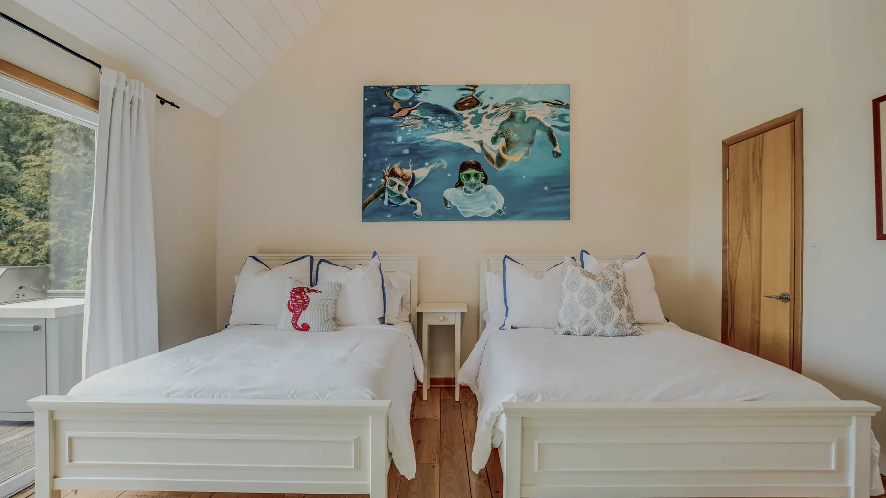 A bright bedroom with two beds and a colorful underwater painting above them.