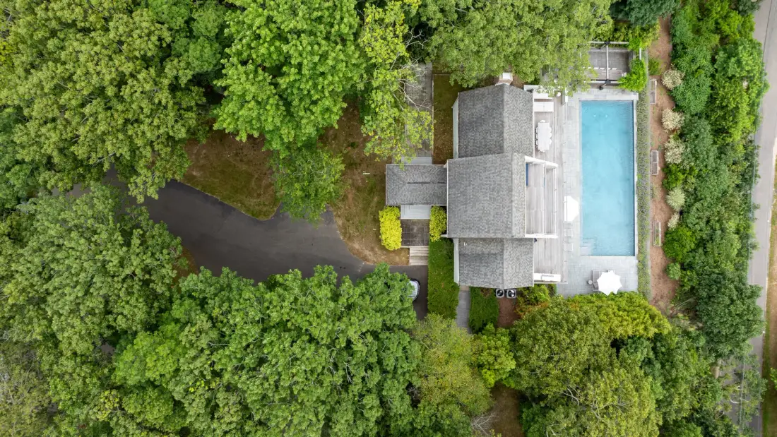 An aerial view shows a building beside a rectangular outdoor swimming pool amid dense greenery.
