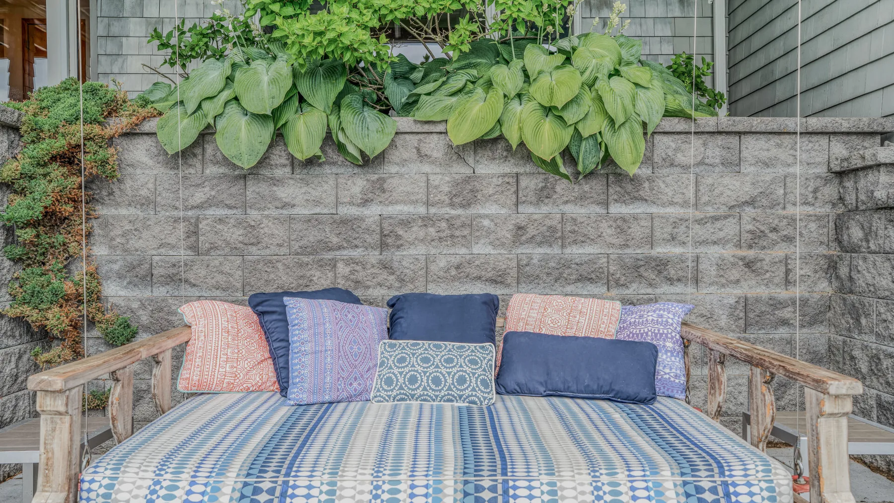 An outdoor seating area with colorful cushions beneath leafy plants.