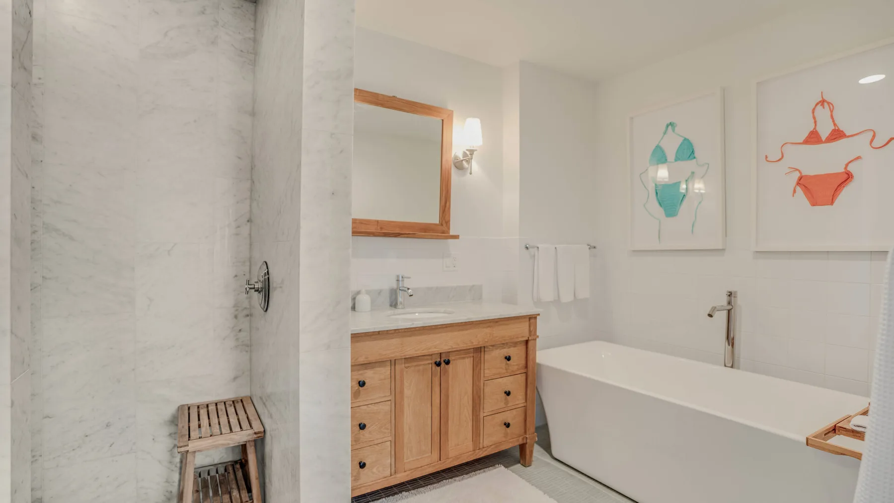 A bright bathroom with a bathtub, wooden vanity, and framed artwork.