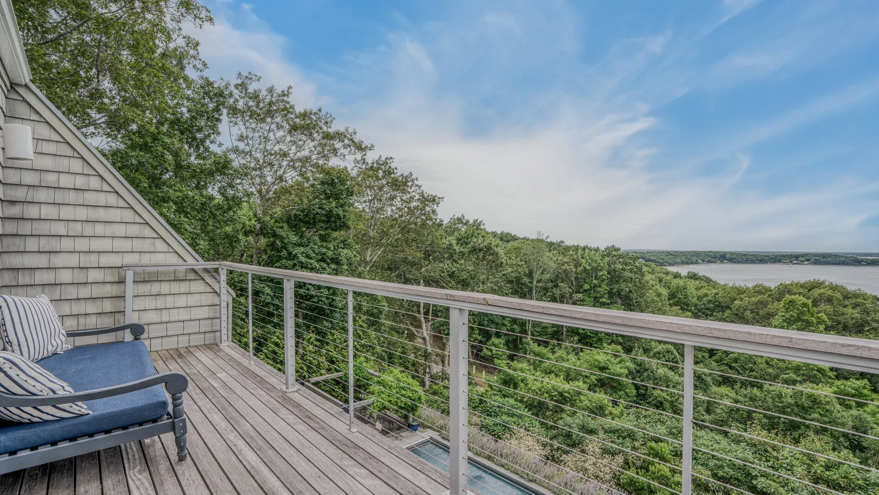 A wooden deck overlooks leafy treetops and a distant stretch of water.