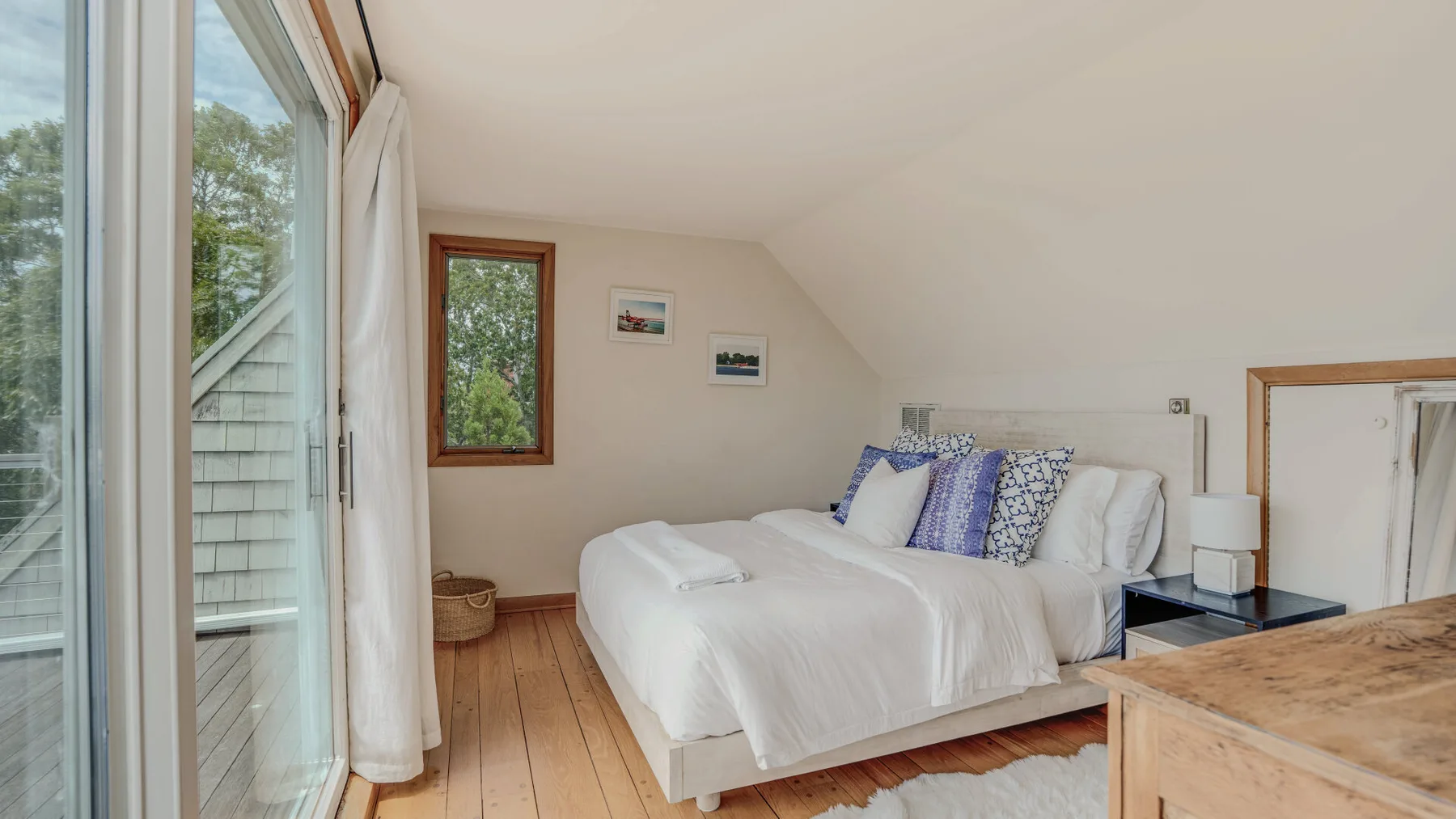 A bright bedroom with a white bed beside large windows.