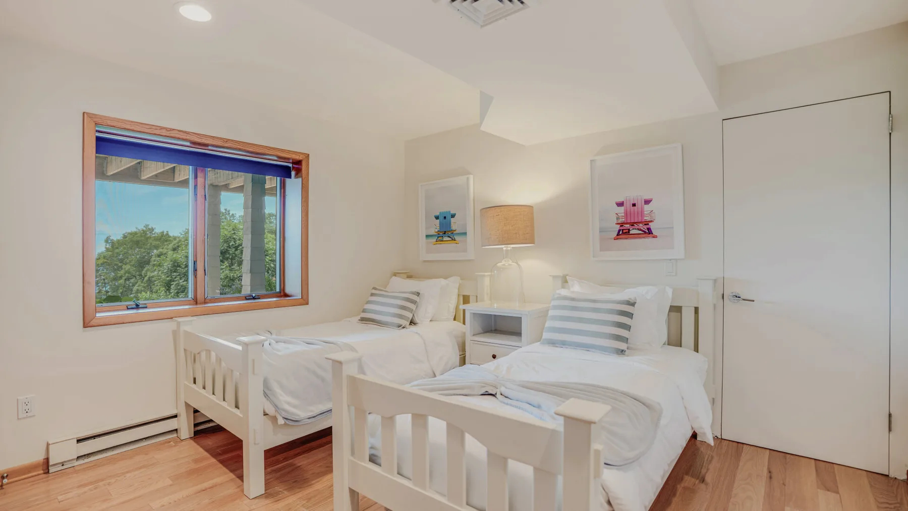 A bright bedroom with two single beds beside a large window.