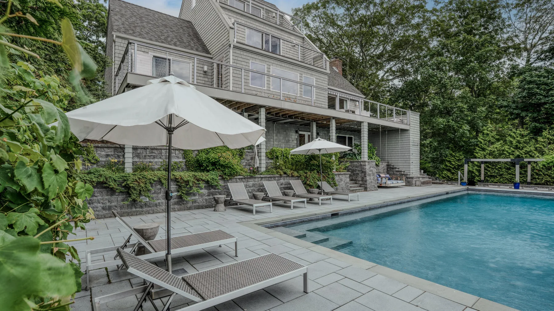 An outdoor swimming pool with lounge seating sits beside a large multi-level house.