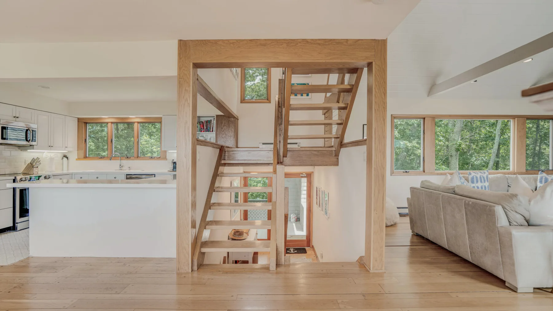 An open-plan living area with a kitchen, seating, and a wooden staircase.