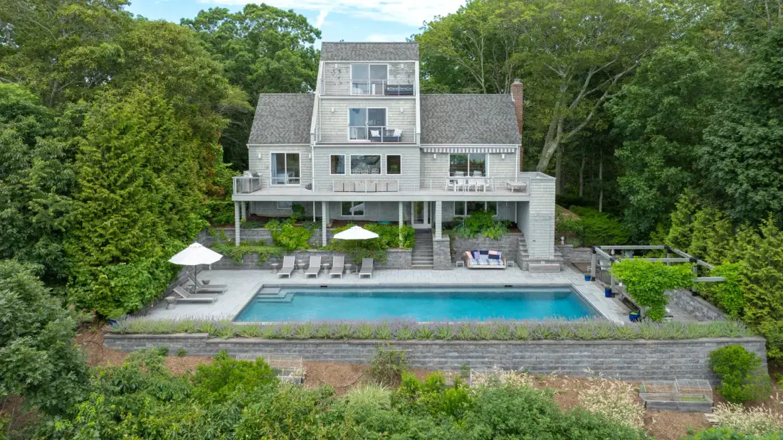 Una casa grande da a una piscina y un jardín con vegetación.