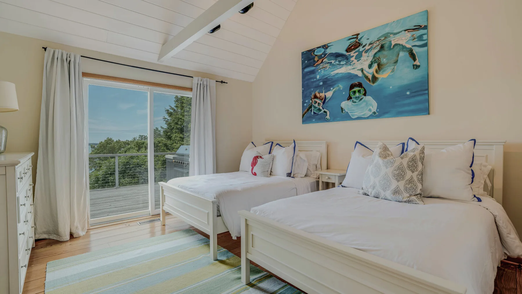 A bright bedroom with two beds, a sliding glass door, and a colorful wall painting.