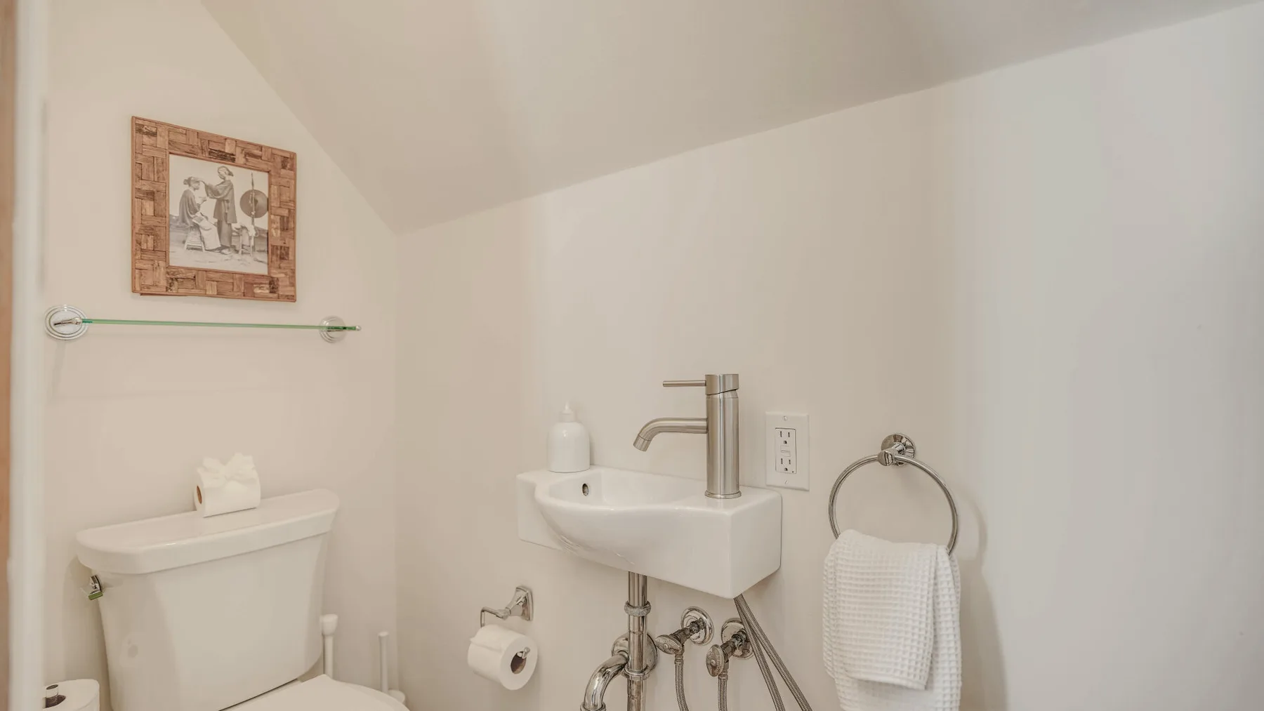 A bathroom with a wall-mounted sink, toilet, and towel ring.