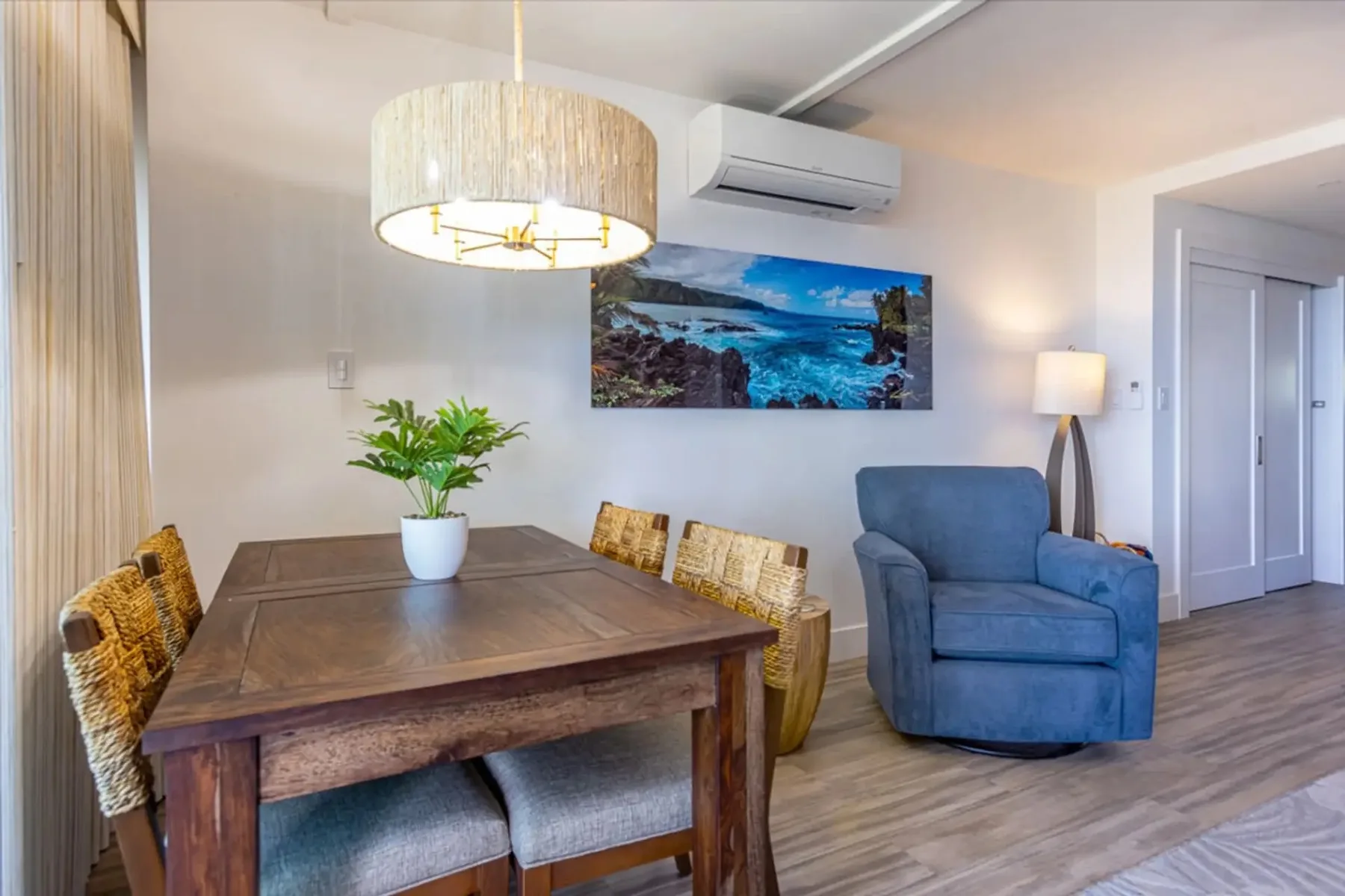 Zona de comedor y estar con una mesa de madera, un sillón azul y arte en la pared.
