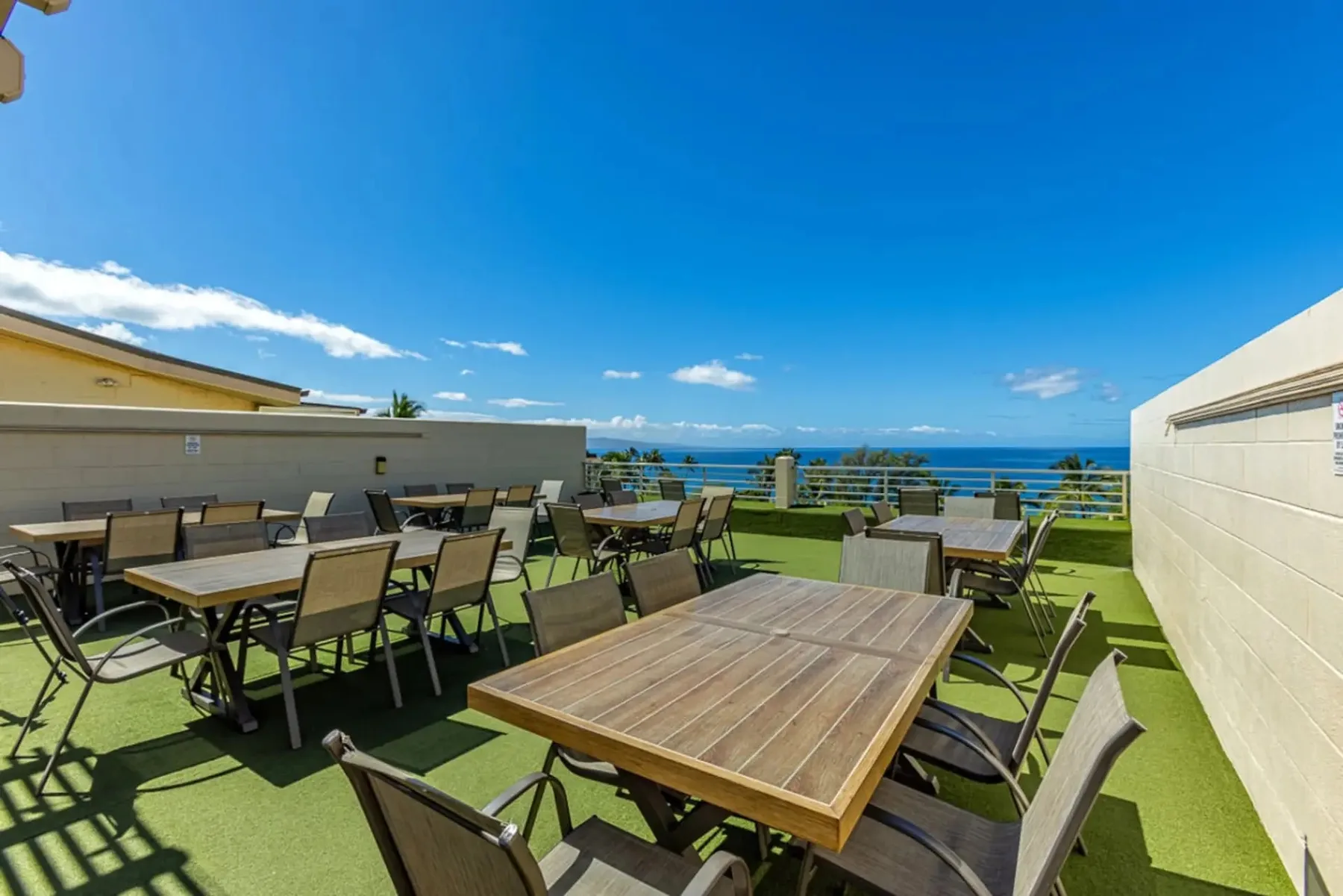 Una terraza exterior con mesas y sillas ofrece vistas al océano.