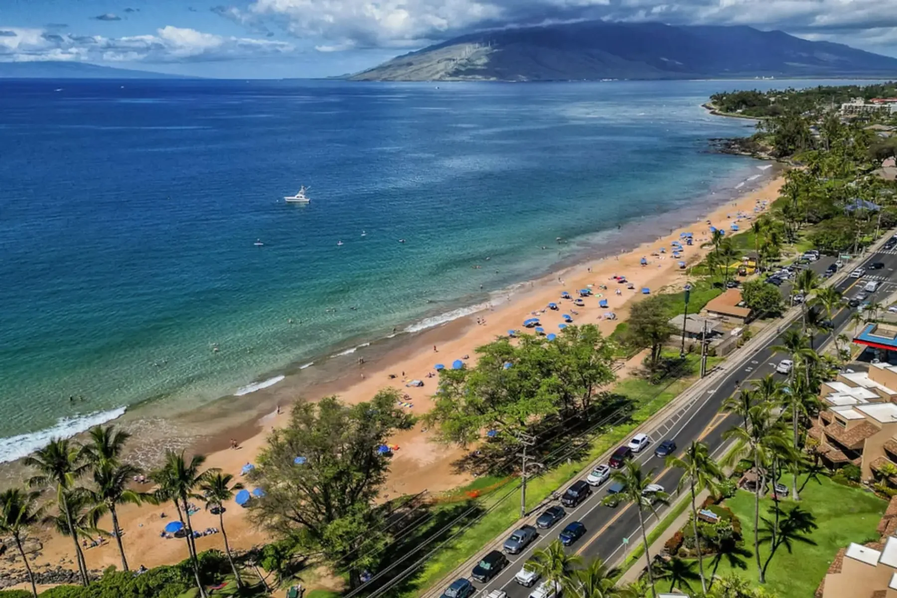Vista aérea de una playa de arena junto a una carretera costera y aguas azules.