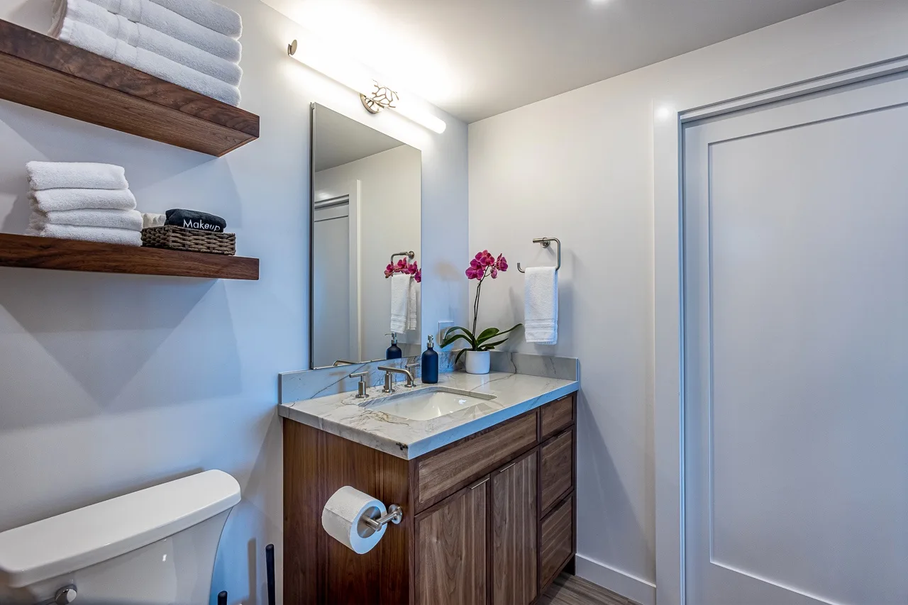Un tocador de baño con espejo, toallas y flores junto a una puerta cerrada.