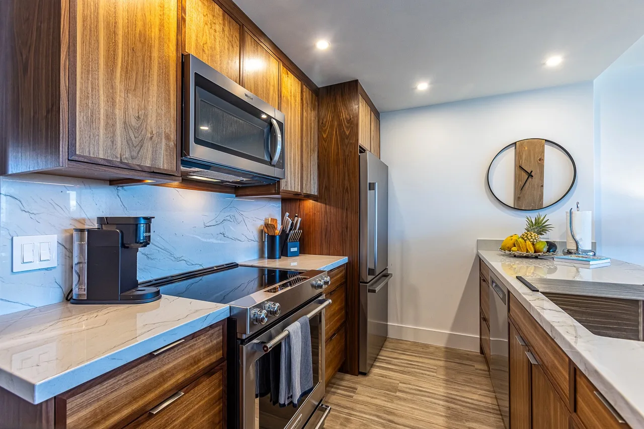 Una cocina moderna con gabinetes de madera, encimeras de piedra y electrodomésticos de acero inoxidable.