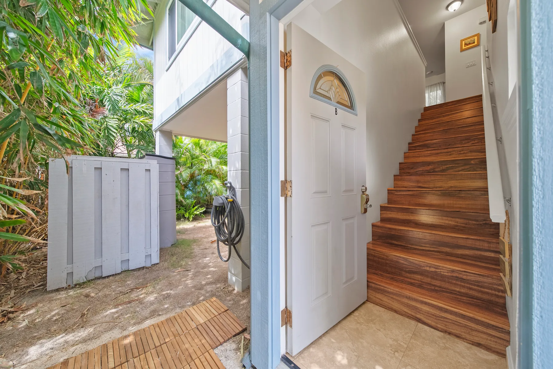 An open entryway leads to a wooden staircase, with a leafy garden visible outside.