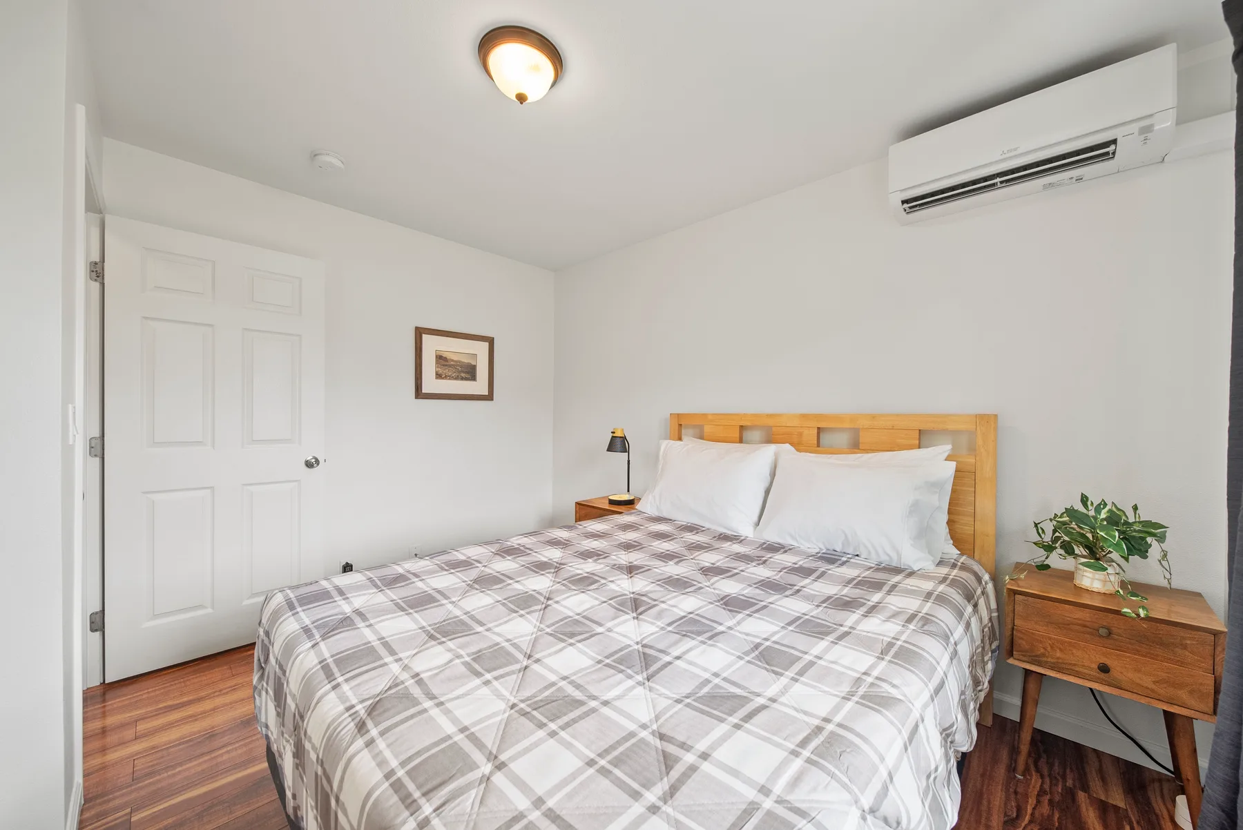 A bedroom with a bed, plaid bedding, and a wooden bedside table.