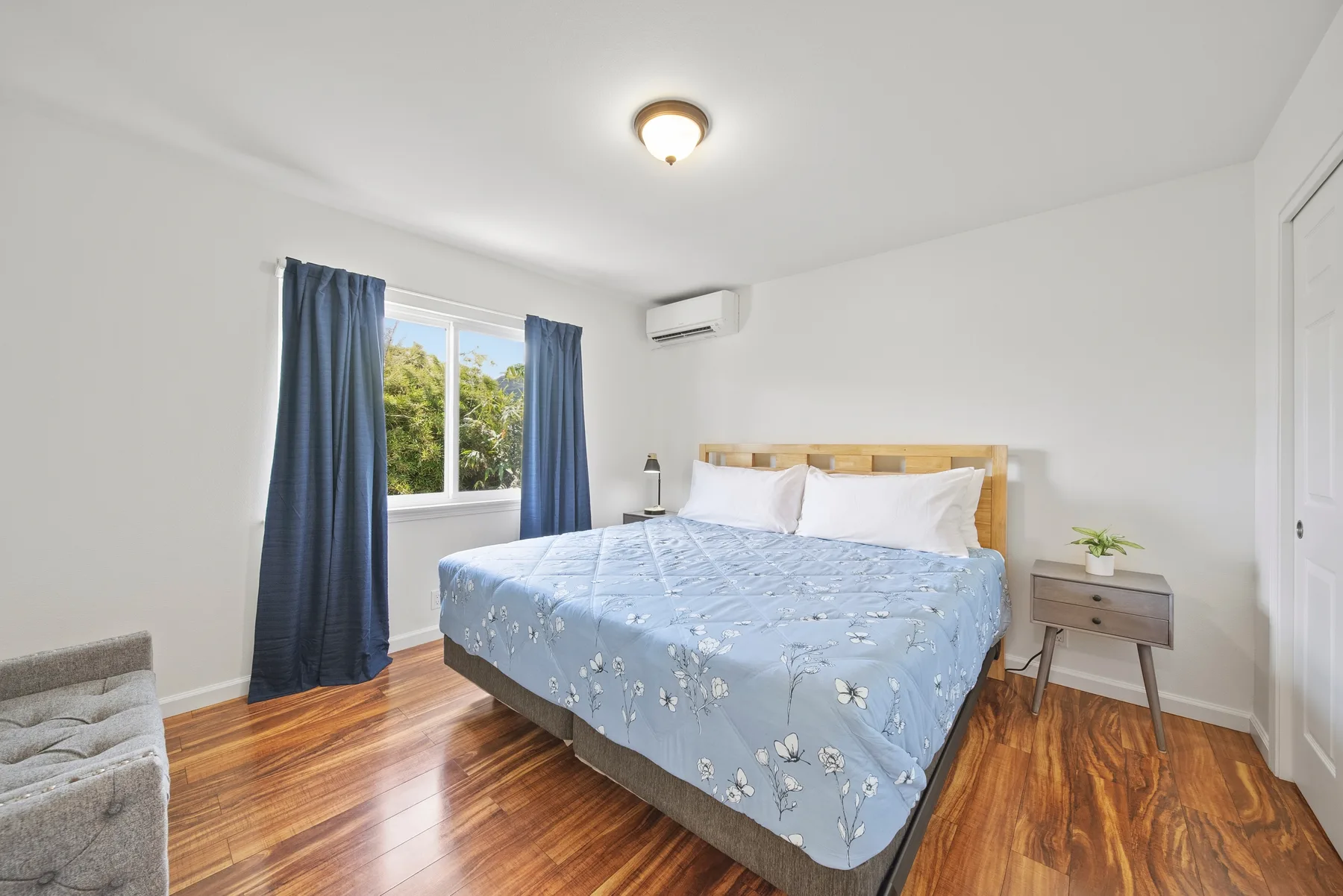 A bedroom with a bed covered in blue floral bedding beside a window.