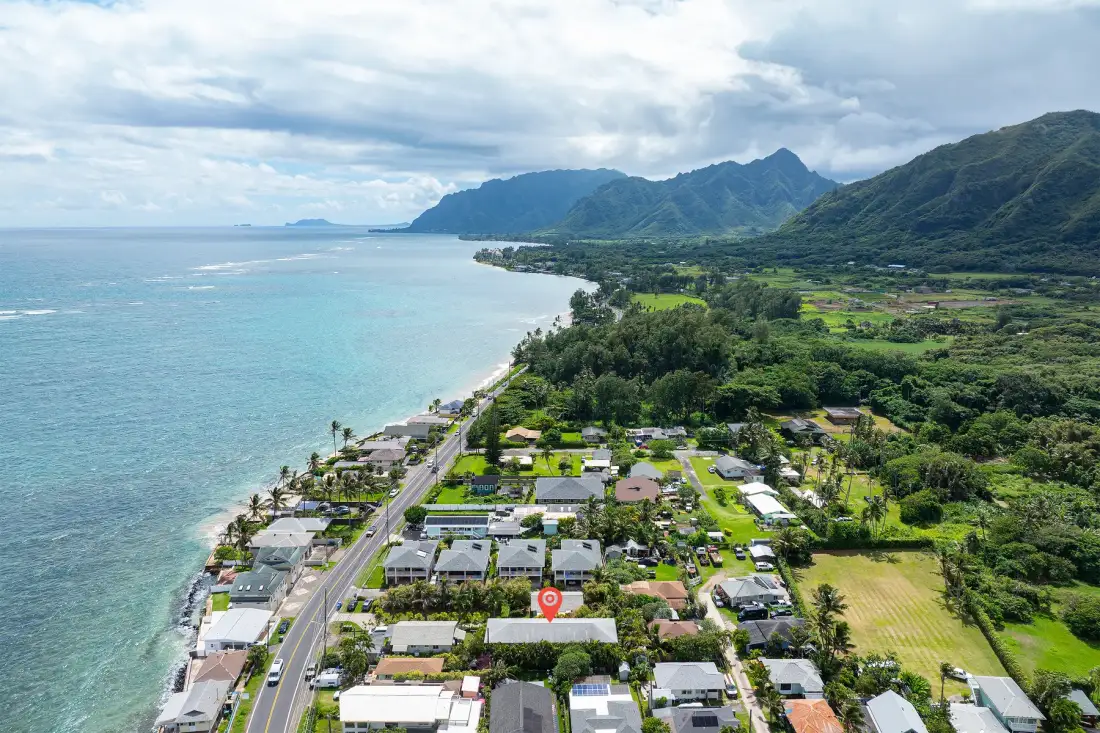 Aerial view of a coastal neighborhood beside the ocean and green mountains.