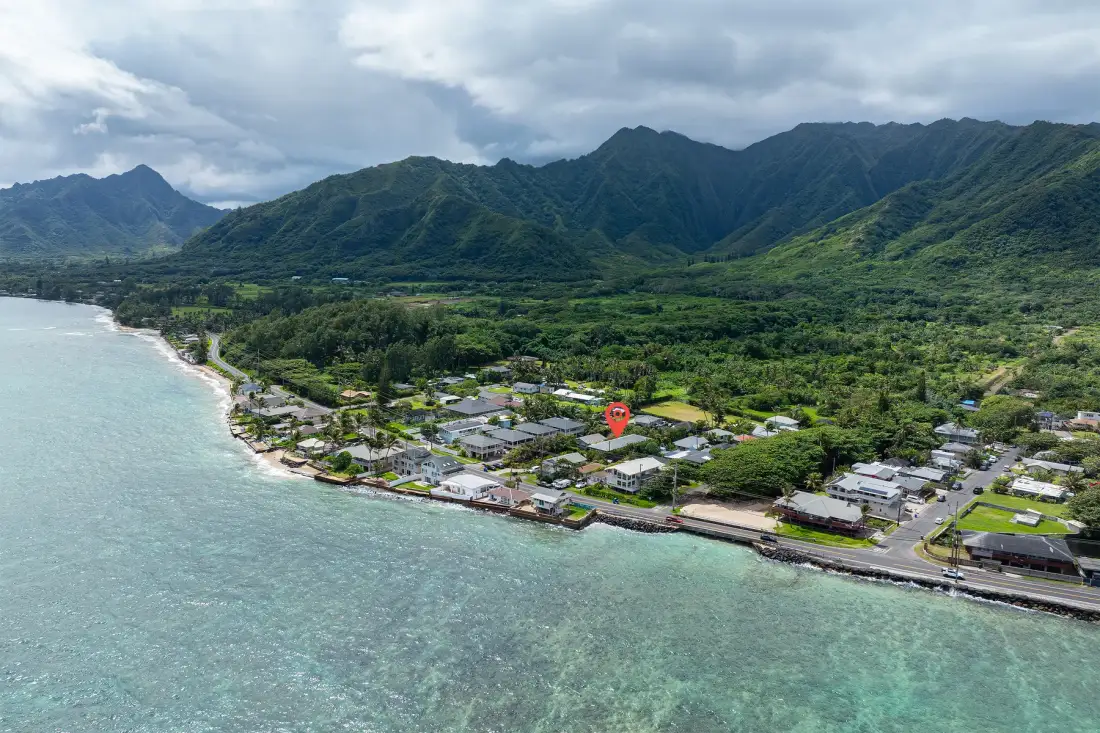 Aerial view of a coastal settlement with green mountains in the background.