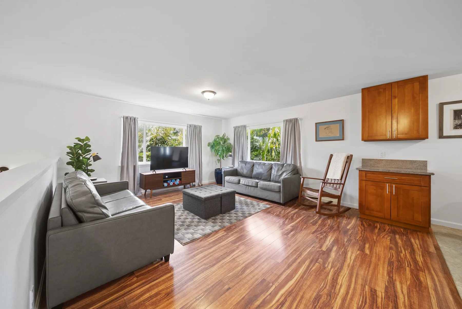 A bright living room with gray seating, a television, and wooden flooring.