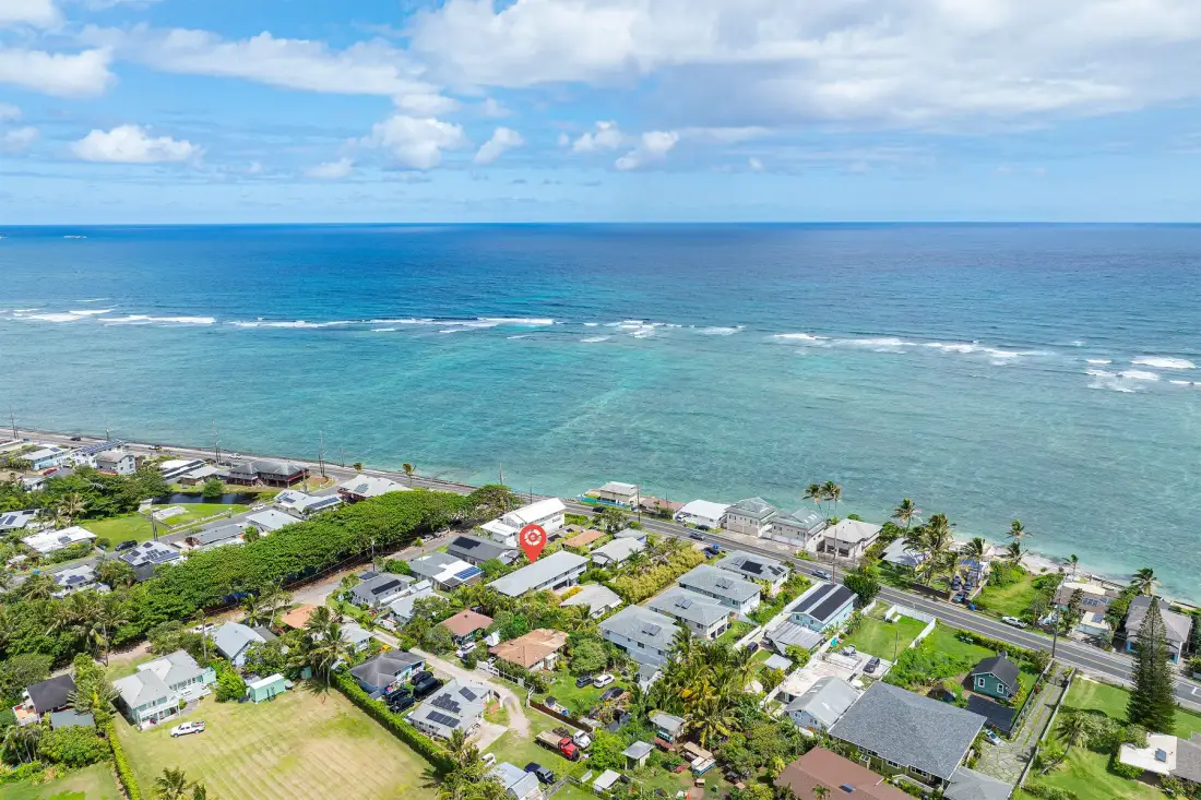 Aerial view of a coastal neighborhood beside the ocean under a partly cloudy sky.