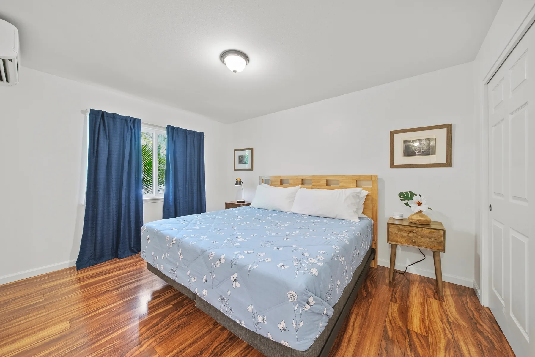 A bedroom with a bed, blue curtains, and wooden flooring.