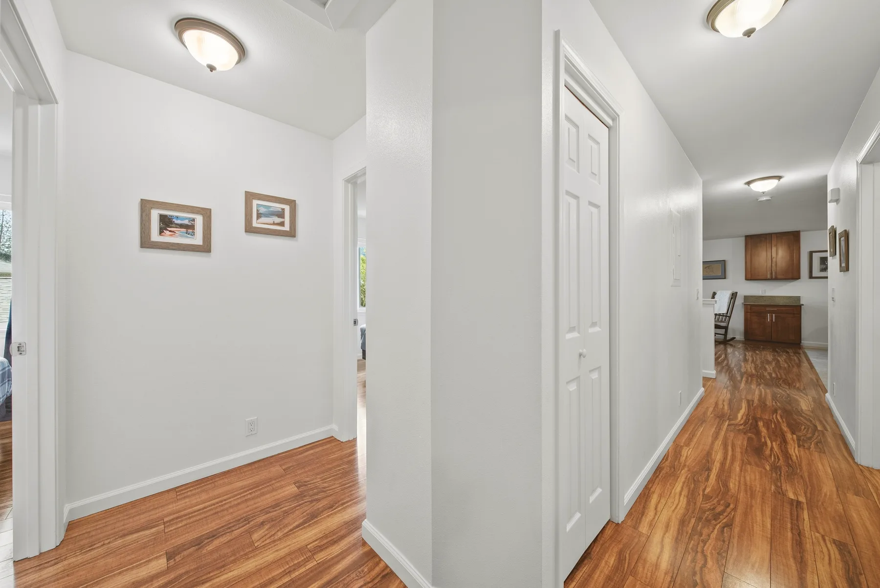 A bright hallway with wood flooring, white walls, and framed pictures.