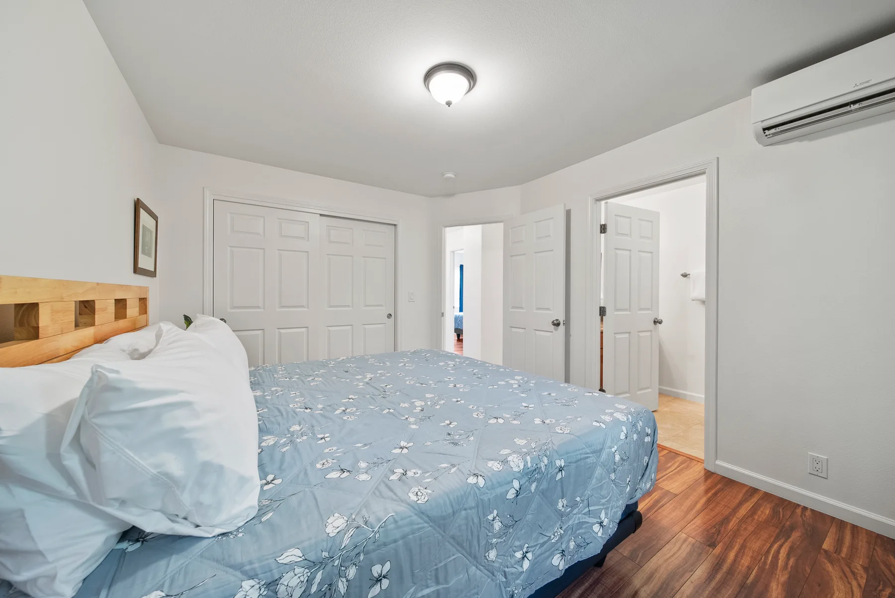 A bedroom with a bed covered in blue floral bedding and white closet doors.