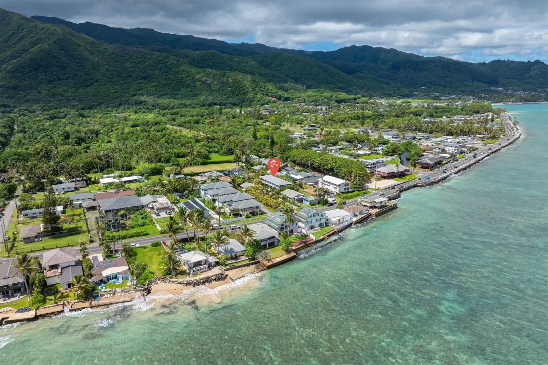 Aerial view of a coastal neighborhood with green mountains in the background.