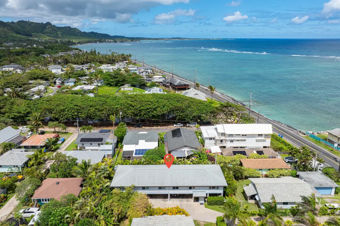 Aerial view of homes and greenery along a coastal road beside the ocean.