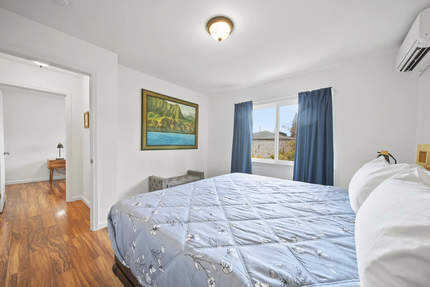 A bedroom with a bed, blue curtains, and a framed landscape painting.