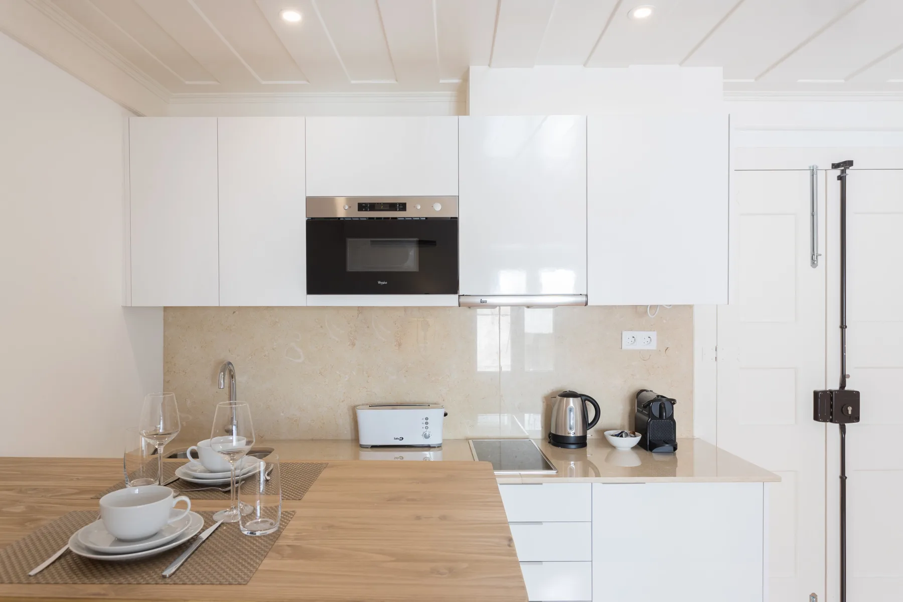 Una cocina luminosa con armarios blancos, electrodomésticos empotrados y una mesa de madera.