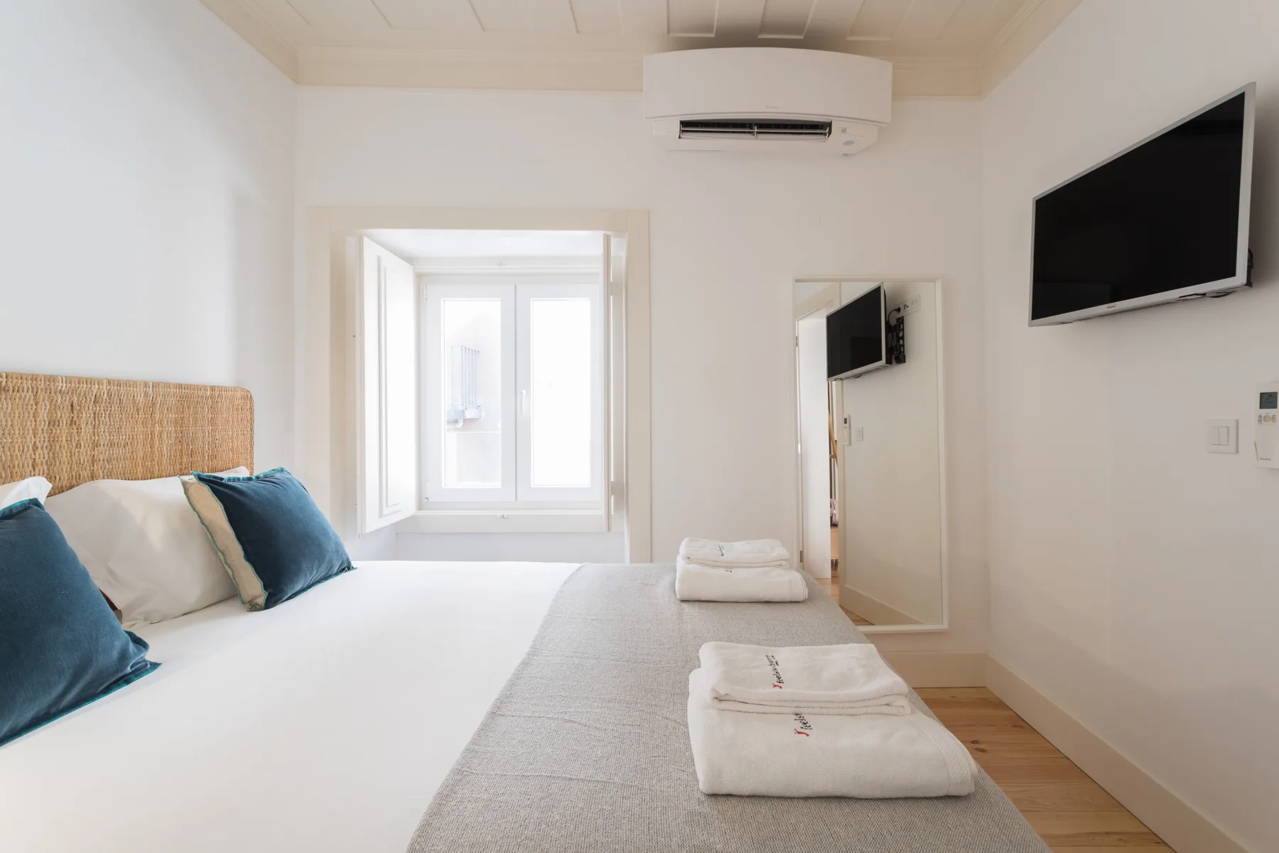 Un dormitorio luminoso con una cama, una ventana y un televisor en la pared.