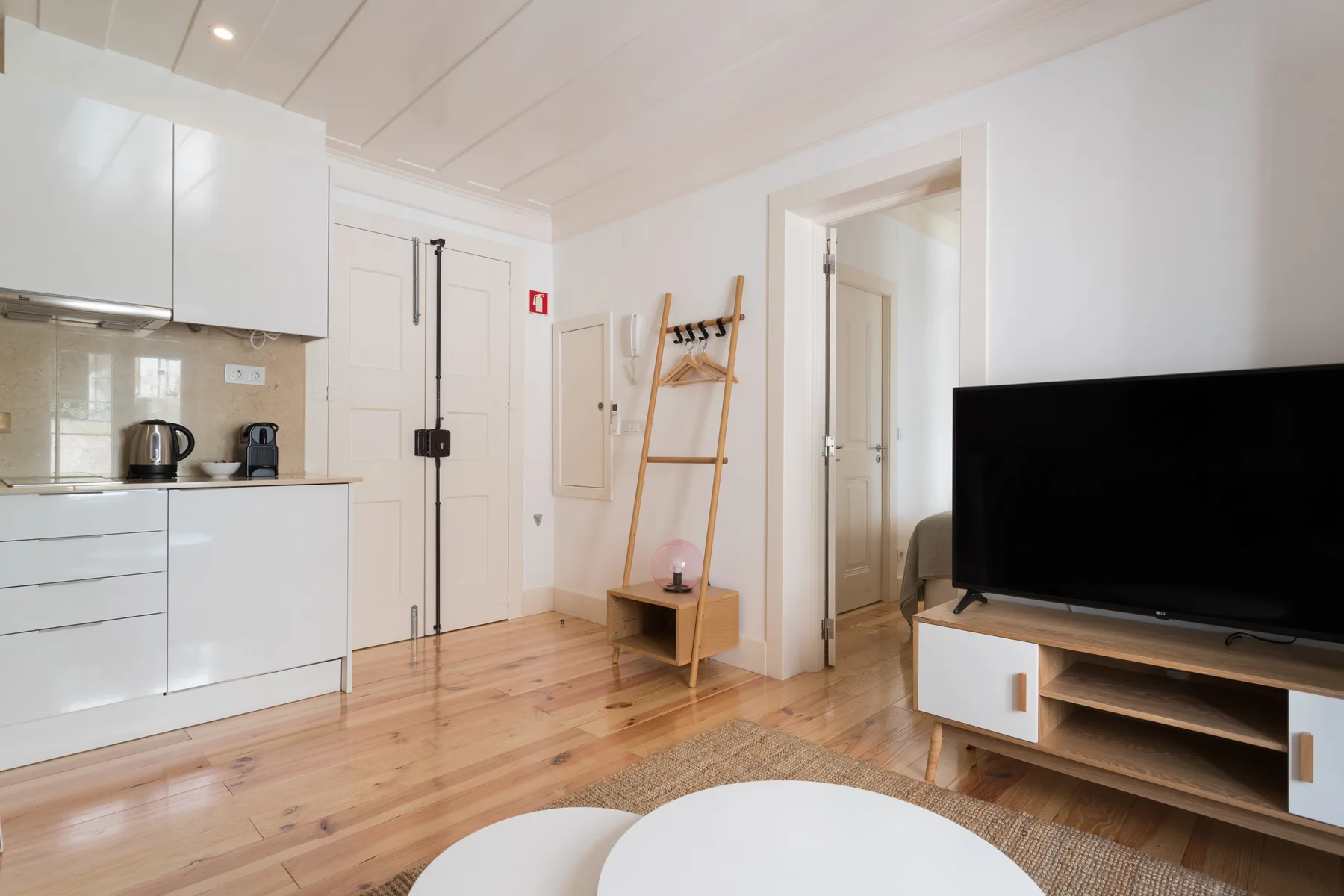 Una luminosa sala de estar con televisor, asientos y una cocina compacta.