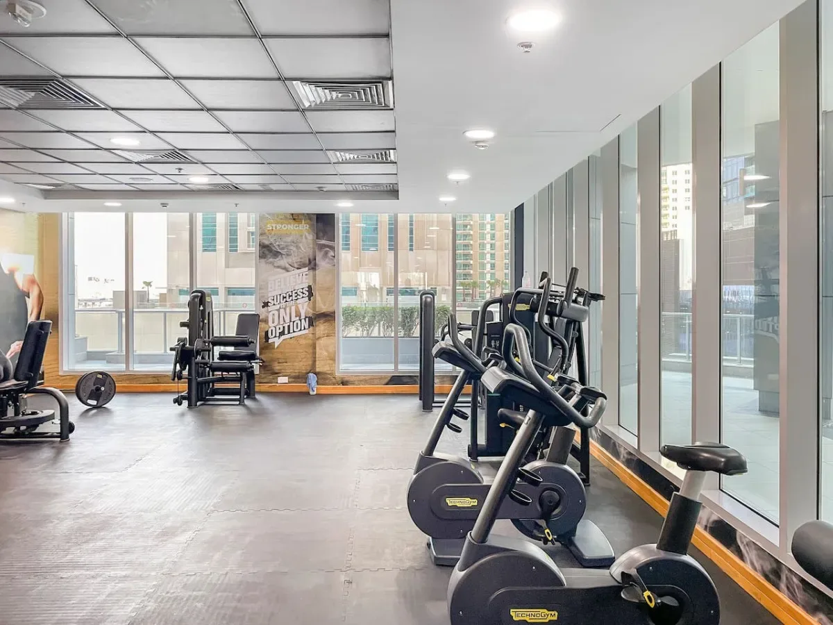 A gym with exercise bikes and other fitness equipment beside large windows.