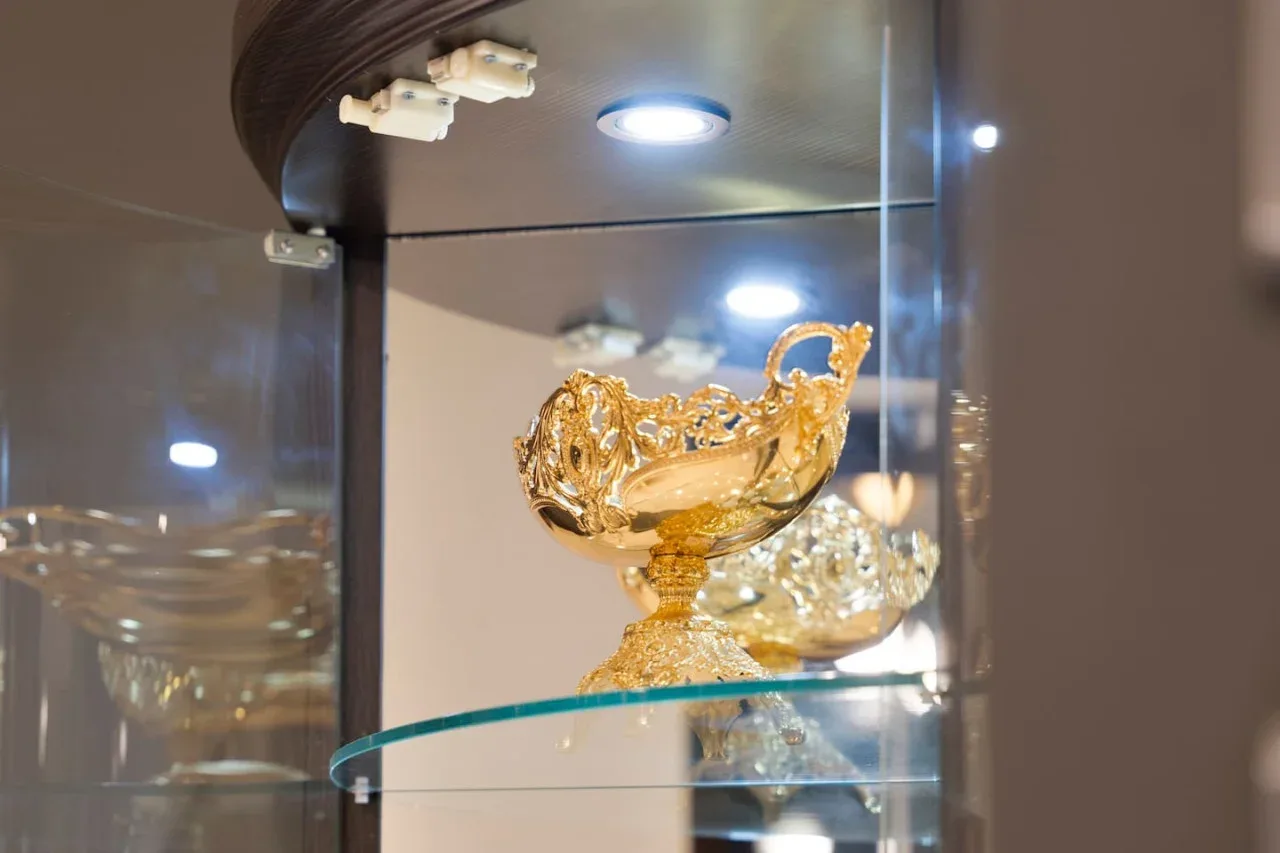 A glass display cabinet showcases an ornate gold-colored decorative bowl.