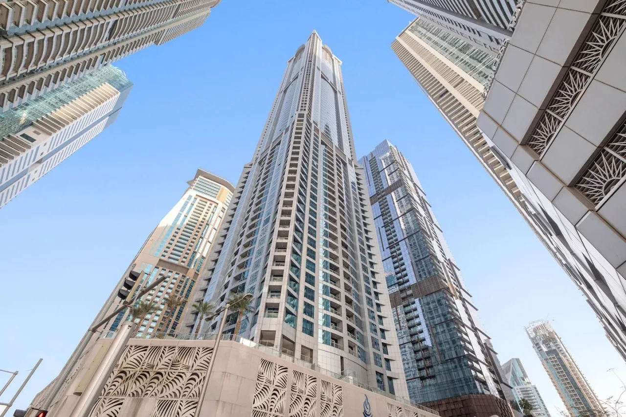 Tall modern buildings rise around a clear blue sky in an upward city view.