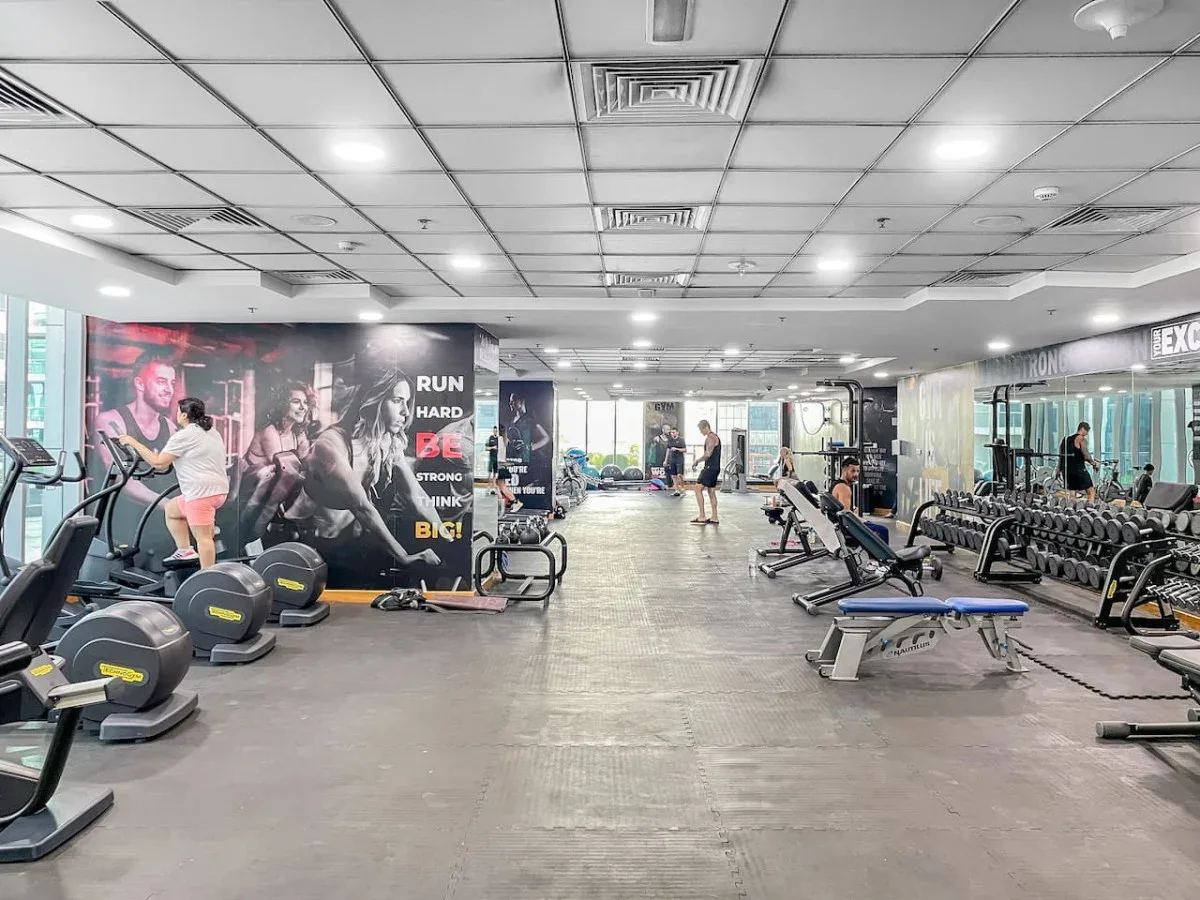 A spacious gym with exercise machines, weights, and people working out.