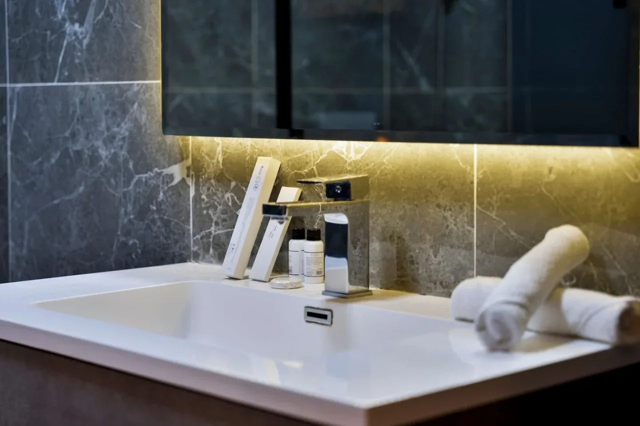 A bathroom vanity with a white sink, toiletries, and folded towels.