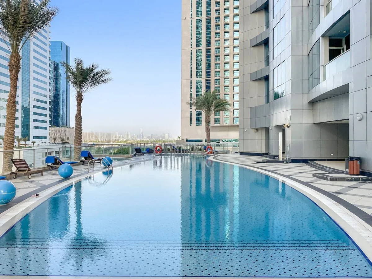 An outdoor swimming pool beside modern high-rise buildings and palm trees.